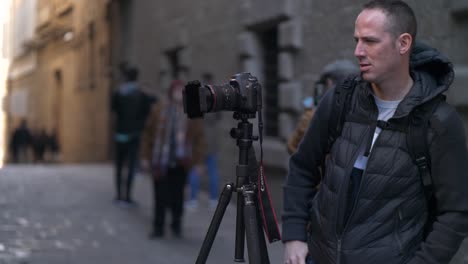 Male-Photographer-with-DSLR-Camera-on-Tripod-Checking-Angle-in-City-Scene