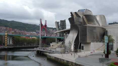 Passanten-Vor-Dem-Guggenheim-Museum-Bilbao-Mit-Puente-De-La-Salve-Im-Hintergrund-In-Bilbao,-Baskenland,-Spanien