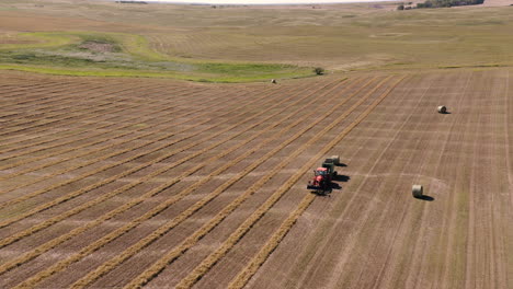 Tractor-Empacando-Heno-En-Las-Tierras-De-Cultivo-En-Saskatchewan,-Canadá-En-Un-Día-De-Verano---Drone-Aéreo,-Tiro-En-órbita