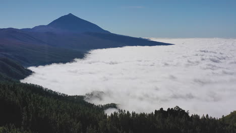 Aerial-shot-of-a-view-from-Pico-de-Teide-on-Canary-Islands-during-a-heavy-cloud-inversion-below-the-mountains-and-forests-and-a-clear-blue-sky-above