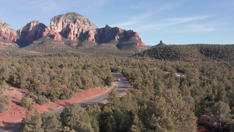 AERIAL:-Shot-in-Sedona-Arizona-of-a-car-driving-through-rock-formations-and-a-beautiful-landscape-on-a-sunny-day