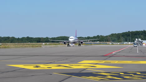 Airplane-Parked-At-The-Airport-Apron-With-Baggage-Car-And-Airport-Baggage-Belt-Loader-Driving-On-The-Side-At-Eindhoven-Airport-In-The-Netherlands
