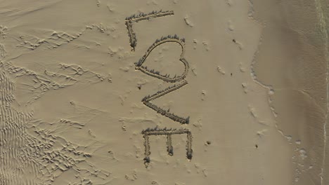 Aerial-crazy-turning-shot-of-LOVE-inscribed-in-the-sand-on-a-beach