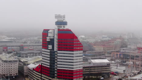Drone-circling-the-lipstick-building-in-Gothenburg,-foggy-day