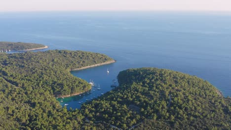 Aerial-view-of-the-Mali-Losinj-island-full-of-pines-and-trees-and-a-small-creek-with-sailboats
