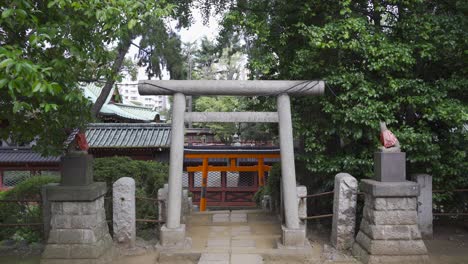 Typical-Japanese-Stone-Torii-Gate-with-backdrop-of-red-Japanese-Temple---frontal-view