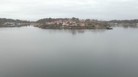 A-tranquil-shot-flying-over-the-still-water-in-Karlskrona,-Sweden-with-the-beautiful-picturesque-island-of-Brandaholm-in-the-background,-with-its-famous-red-cabins