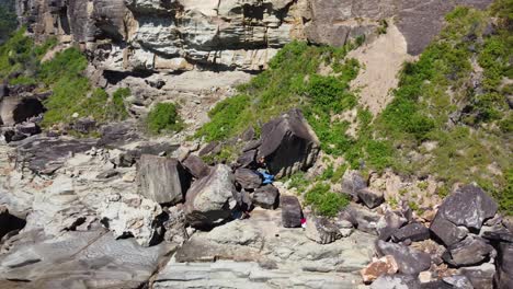 Aerial-drone-scenic-shot-of-bouldering-rock-climber-scaling-rock-sport-recreation-outdoor-rock-climbing-Winnie-Bay-Copacabana-Avoca-Central-Coast-NSW-Australia-4K