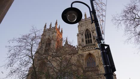 Slow-wide-reveal-shot-of-York-Minster-cathedral-at-sunrise-through-the-the-trees-and-lamp-posts-on-city-street