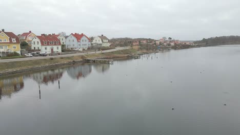 Aerial-view-of-the-still-water-in-Karlskrona,-Sweden-with-a-group-of-birds-in-the-water-and-a-man-running-by-the-coastline,-with-typical-swedish-houses-in-the-background