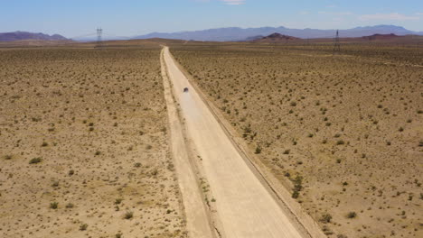 Black-SUV-speeds-down-a-straight-dirt-desert-road-leaving-a-dust-cloud-behind