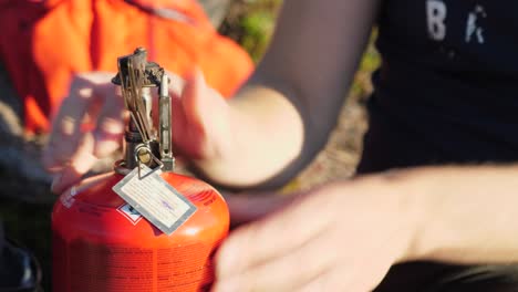 Close-up-profile-shot-of-person-opening-metal-pan-holder-on-a-orange-propane-camping-fuel-heater,-outdoors-in-a-camping-environment