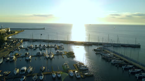 Scenic-Sunrise-View-Over-Marina-Gdynia-In-Gdynia,-Poland-With-Boats-And-Yachts-Moored-On-The-Calm-Sea-At-The-Baltic-Coast---pullback-drone-shot