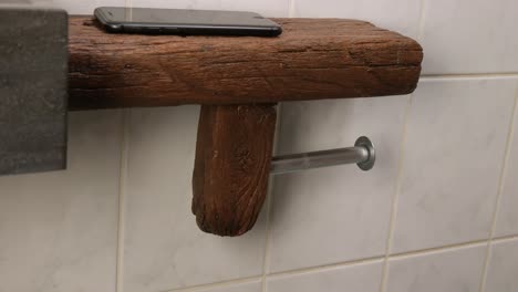 Eine-Aufnahme-Eines-Kaukasischen-Mannes,-Der-Sein-Smartphone-Auf-Ein-Regal-In-Einem-Toilettenraum-Stellt-Und-Leeres-Toilettenpapier-Gegen-Eine-Neue-Rolle-Toilettenpapier-Austauscht