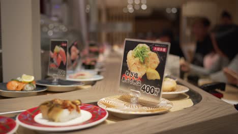 Plates-Of-Sushi-On-The-Moving-Conveyor-Inside-Kaitenzushi-Restaurant-In-Kyoto,-Japan---close-up,-selective-focus