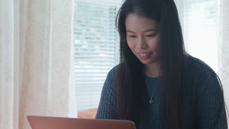 Joven-Asiática-Americana-Escribiendo-En-Una-Laptop,-Sonriendo,-A-Cámara-Lenta