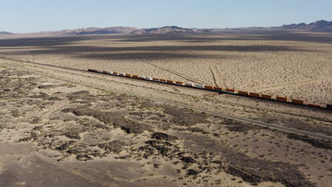 Extremely-long-freight-train-with-many-train-cars-speeds-down-a-train-track-through-a-desert-landscape