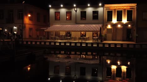Vista-Nocturna-De-Un-Canal-Con-Restaurantes-Y-Gente-Adentro-Y-Una-Iluminación-Cálida