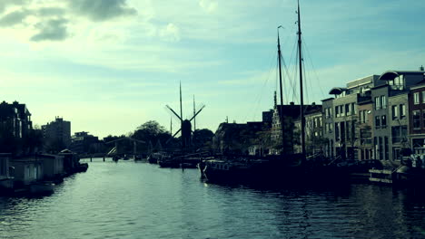 Zeitrafferaufnahme-Des-Kanals-In-Leiden-Mit-Vorbeifahrenden-Booten-An-Sonnigen-Tagen-Und-Windmühle-Im-Hintergrund
