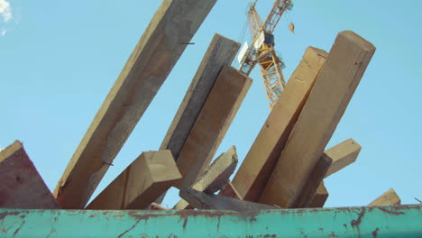 Logs-of-a-construction-site-protrude-from-a-container-with-a-construction-crane-in-the-background