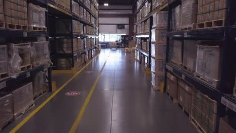 Forward-aerial-shot-of-boxes-on-tall-shelves-in-industrial-warehouse