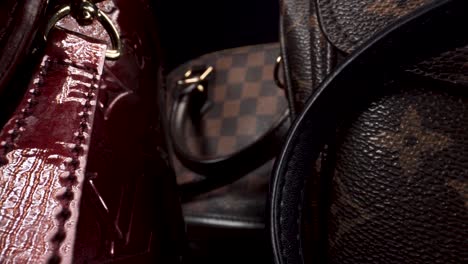 macro-view-moving-backward-past-expensive-luxury-leather-bags-in-dark-scene,-Louis-Vuitton,-probe-lens