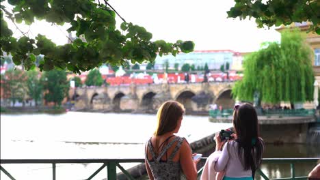 Two-girls-taking-photos-of-Charles-Bridge-in-Prague,-sunny-day-slow-motion-static-view