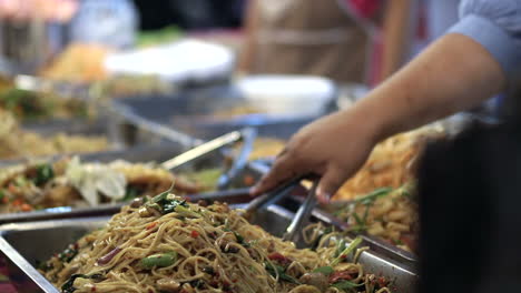 Primer-Plano-De-La-Persona-Que-Prepara-Fideos-Fritos-Tradicionales-En-El-Mercado-De-Comida-Callejera-Durante-La-Noche-En-Bangkok