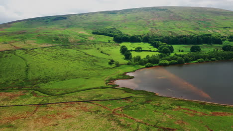 Aerial-shot-of-a-lake-surrounded-by-green-countryside,-on-a-bright-summers-day