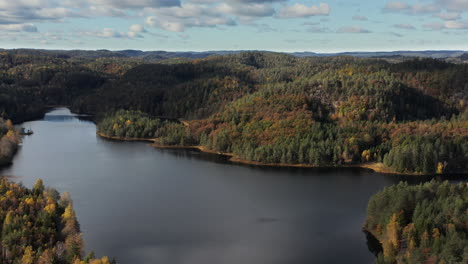 Aerial-view-of-a-lake,-surrounded-by-hills-and-foliage-forest,-in-Norway---Reverse,-tilt,-drone-shot