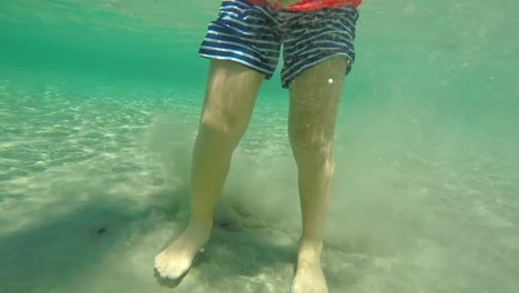 Underwater-footage-of-caucasian-kid,-swimming-with-a-swim-board-60fps,-at-clear-green-sea-at-Greece