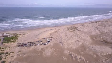 Aerial-tilting-up-seascape-shot-of-Birubi-Beach-sand-dunes-desert-and-camel-rides-attraction-at-Stockton-Beach-with-ocean-horizon-in-the-background