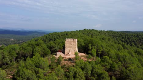 Beautiful-historic-European-Stone-watchtower-in-the-middle-of-a-dense-beautiful-Green-forest-surrounded-by-mountains,-Drone-Aerial