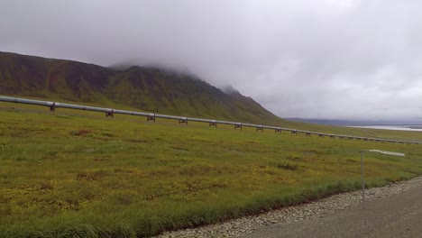 POV-shot-to-the-side,-while-driving-on-the-Dalton-Highway,-of-the-Trans-Alaska-Pipeline-System,-on-a-dark,-gloomy,-fall-day,-in-Alaska,-USA