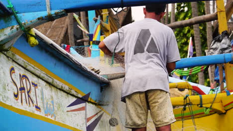 Pescador-Arreglando-La-Red-Junto-A-Una-Canoa-De-Apoyo-Indonesia