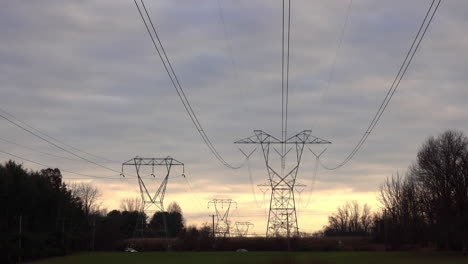 Long-shot-of-electrical-transmission-towers-stretching-into-the-distance-against-somber-cloudy-sky-at-sunset
