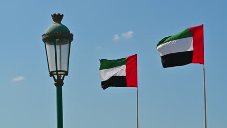 4k-Aufnahmen:-Zwei-Nationalflaggen-Der-Vereinigten-Arabischen-Emirate-Wehen-Im-Wind-Gegen-Den-Klaren-Blauen-Himmel,-Ein-Teil-Der-Feierlichkeiten-Zum-Nationalfeiertag-Der-Vereinigten-Arabischen-Emirate