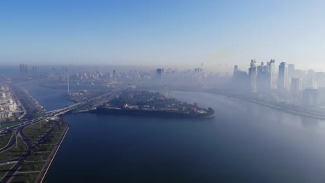 View-from-above-of-Sharjah's-Khalid-Lake,-Eye-of-Emirates,-Sharjah-Skyline-on-a-foggy-morning,-Fog-in-Gulf,-United-Arab-Emirates,-4K-video