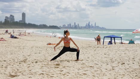 Woman-Practicing-Yoga-And-Doing-Extended-Side-Angle---Surfers-Paradise-From-Burleigh-Heads-Beach-In-QLD,-Australia