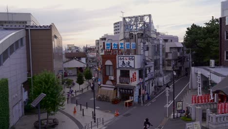Typisches-Wohngebiet-In-Einer-Japanischen-Stadt-Mit-Schaufenstern-Und-Menschen,-Die-Bei-Sonnenuntergang-Auf-Fahrrädern-Fahren