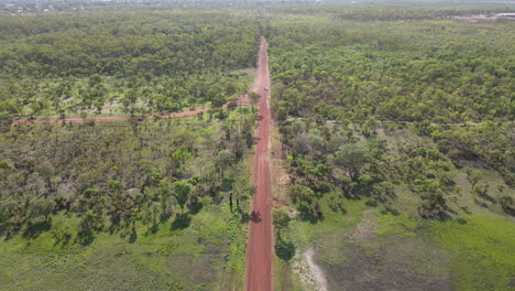 High-Slow-Moving-Aerial-Drone-shot-of-Long-Straight-Red-Road-and-Green-Bushland-Near-Holmes-Jungle-Nature-Park,-Darwin,-Northern-Territory