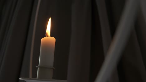 Close-view-of-lit-candle-on-hanging-holder-moving-in-front-of-curtains