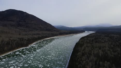 Icy-Liard-river-in-Canada-at-winter-with-cloudy-forest,-aerial-drone