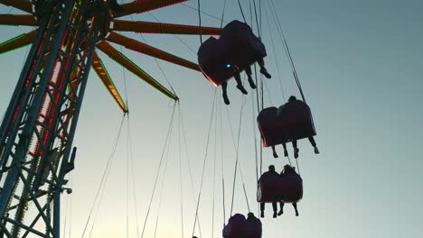 Low-angle-view-of-fair-chain-swing-ride-at-dusk-spinning-around-people,-static
