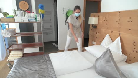 A-maid-with-face-mask-cleans-the-hotel-room-and-makes-the-bed