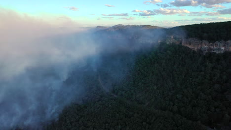 Smoke-clouds-floating-above-forest-landscape-during-bushfires,-forward-aerial
