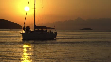 Sunset-at-Vela-Luka,-Croatia,-with-a-sailboat-and-motorboat-crossing-the-view