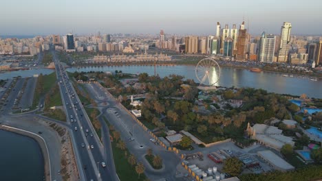 Drone-view-of-Sharjah's-Khalid-Lake-and-city-skyline-on-a-beautiful-evening,-Eye-of-Emirates-Wheel,-Travel-tourism-business-in-the-United-Arab-Emirates