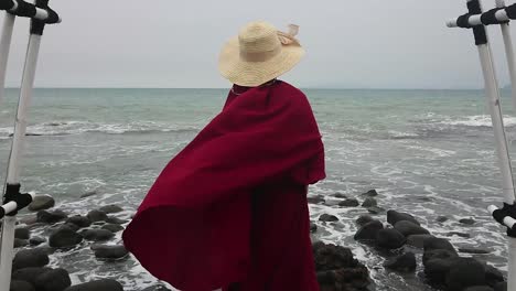 Islamic-woman-wearing-burqa-during-holiday-at-rocky-beach,-puts-on-straw-hat