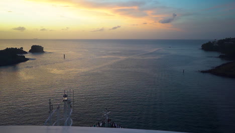 Scenic-view-from-the-board-of-a-cruise-ship-sailing-through-the-calm-Caribbean-sea-in-the-evening,-golden-sunset-in-the-distance-to-the-left,-cliffs-and-buoys-on-both-sides,-scenic-static-FHD-shot
